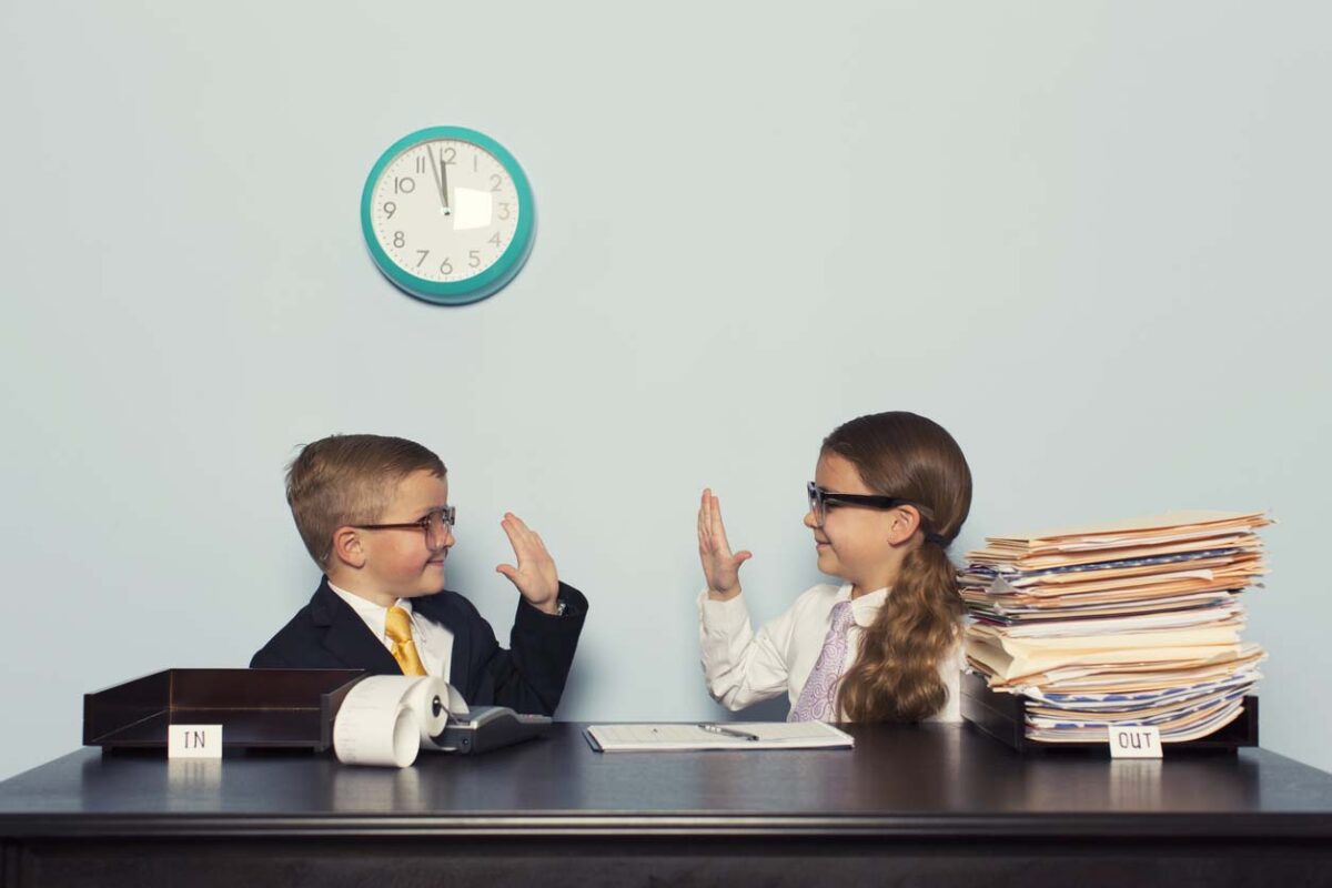 a boy and a girl sitting at a desk in front of a clock.