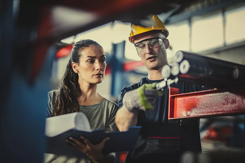 a man and woman in hardhats looking at a piece of paper.